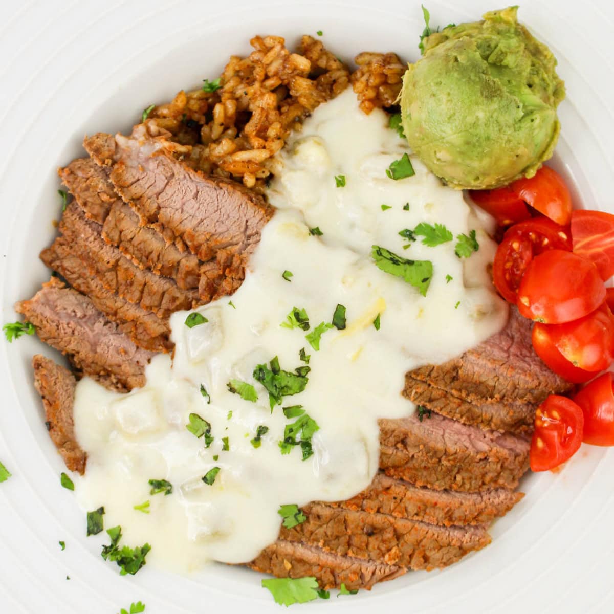 Close up of a Steak and Rice Bowl with cheese sauce, guacmole, and chopped tomatoes.
