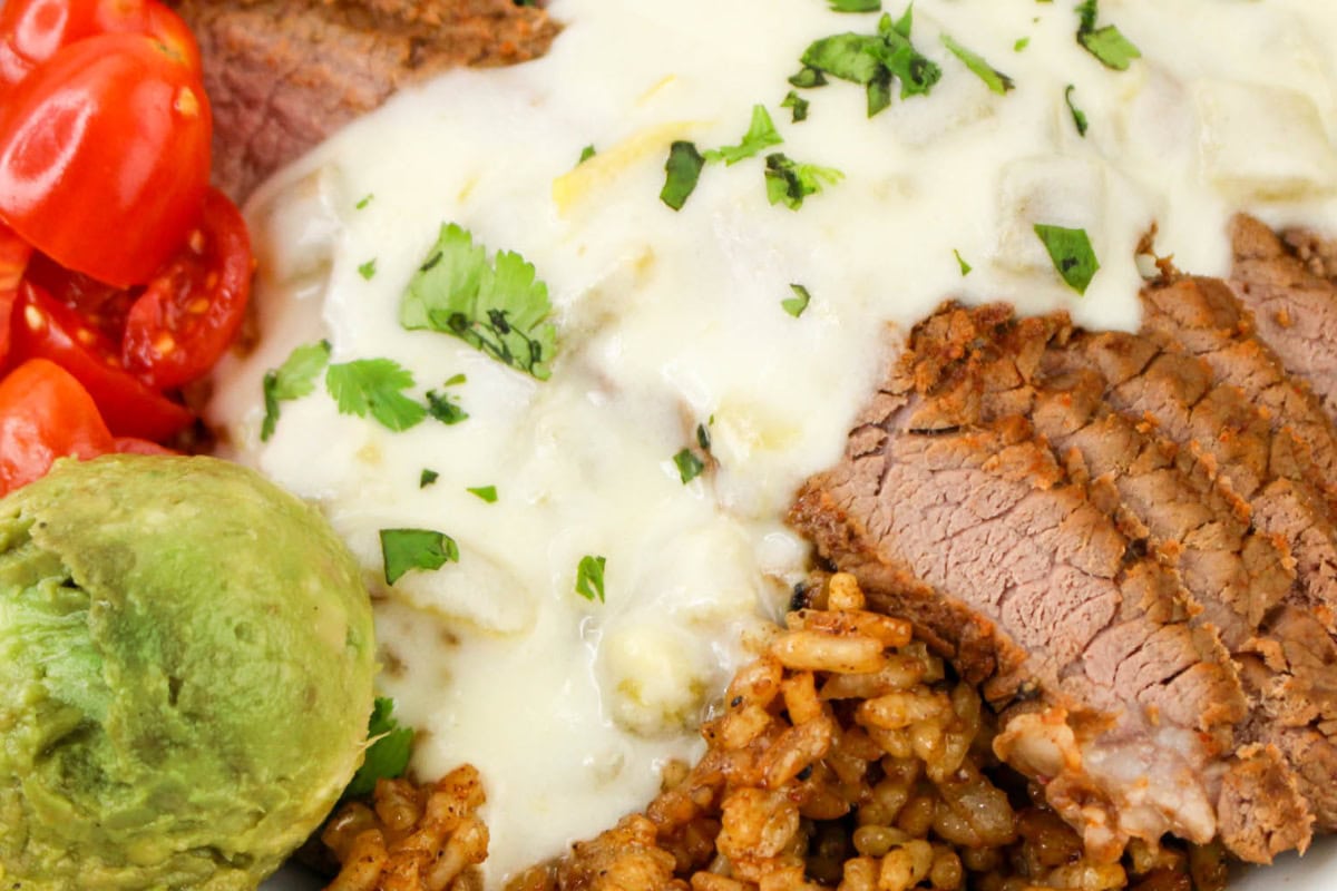 Close up of Steak and Rice Bowl with queso cheese sauce, guacmole, and chopped tomatoes.