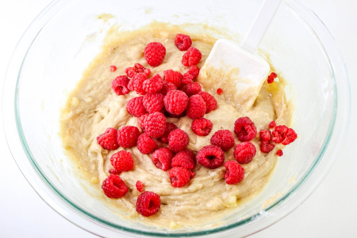Bowl of banana muffin batter with fresh raspberries.