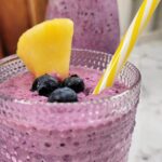 Close up of Blueberry Pineapple Smoothie and a straw, garnished with fresh fruit.